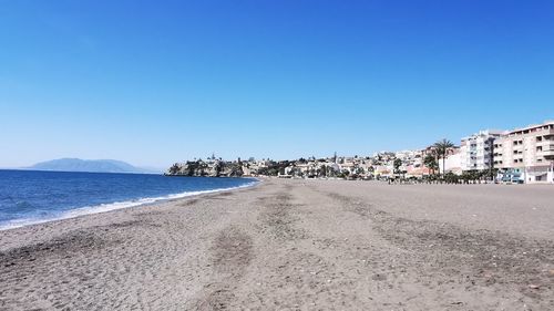 Scenic view of beach by city against clear blue sky