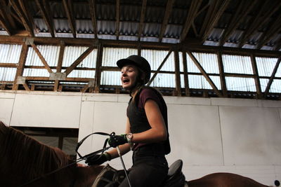 Low angle view of happy female jockey riding horse at stable