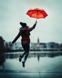 Rear view of woman holding umbrella sea rain flying