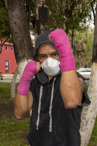 Portrait of man wearing flu mask standing by tree trunk