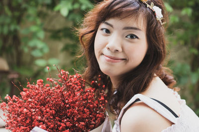 Close-up portrait of smiling woman with red flowering plants