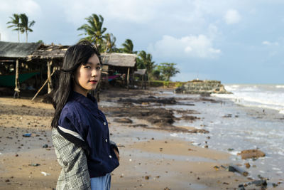 Young woman standing at beach against sky