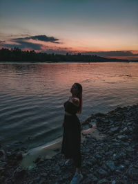 Woman standing on beach against sky during sunset