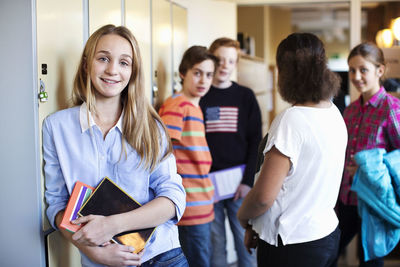Portrait of school girl standing at locker room with friends in background
