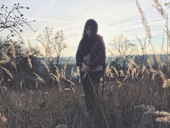 Young woman standing on grassy field against sky during sunset