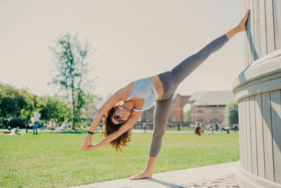 Woman with arms raised on grass against clear sky