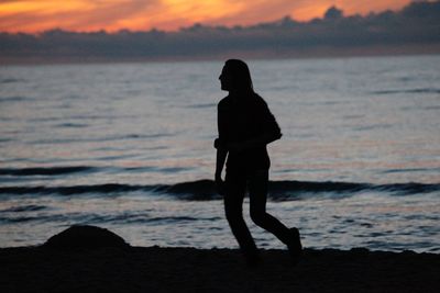 Silhouette man walking on seashore during sunset