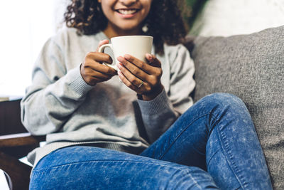 Woman drinking coffee while relaxing on sofa at home