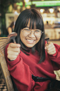 Funny face of asian teenager raise fork and spoon in dinning room