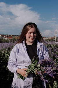 Beautiful young woman standing by purple flowering plants against sky