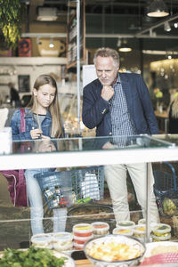 Father and daughter looking in display cabinet while shopping at supermarket