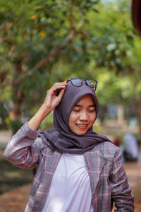 Portrait of young woman standing against trees