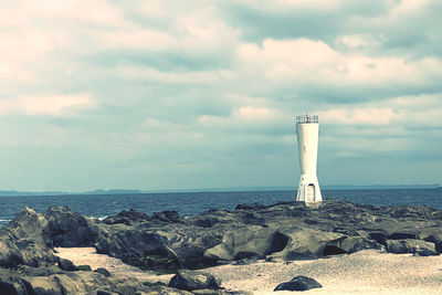 Lighthouse on rocks by sea against sky