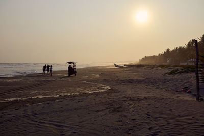 People at beach against sky during sunset