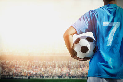 Midsection of soccer player holding ball while standing in stadium