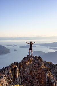 Man standing on rock by sea against sky