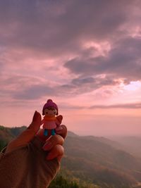 Midsection of person holding orange against sky during sunset