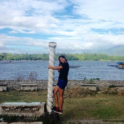 Full length of young woman standing on retaining wall against sea