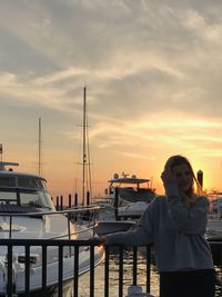 Portrait of woman standing at harbor against sky during sunset