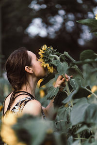 Young european woman with braided hair in a floral dress smelling on a sunflower in a field. 
