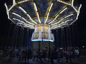 Illuminated chain swing ride in amusement park at night