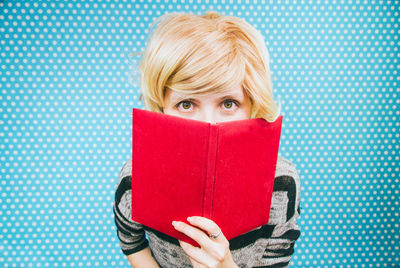 Portrait of woman holding red book against blue polka dots wall