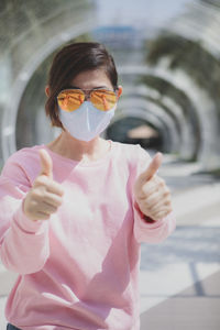 Portrait of woman with sunglasses gesturing while standing outdoors