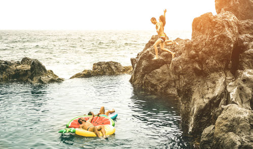 People sitting on rock by sea against sky