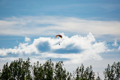 Mid distance view of person paragliding against cloudy sky