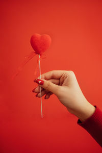 Cropped hand of woman holding red flower against yellow background