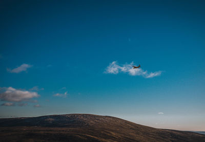 Airplane flying over mountain against blue sky