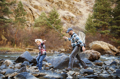 Father and son walking on rocks amidst river by mountain