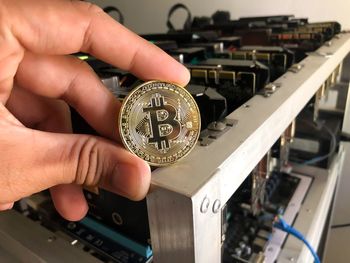Cropped hand holding bitcoin against machine