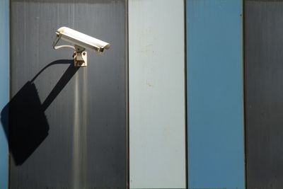 Security camera mounted on exterior building wall, casting shadow in sunlight