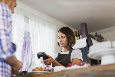 Serious baker using credit card reader while man standing at cafe counter