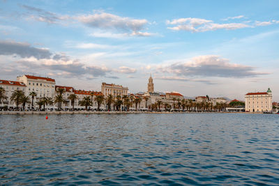 View of city at waterfront against cloudy sky