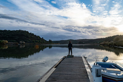 Man standing on pier over lake against sky