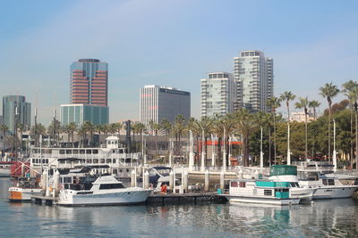 Sailboats moored on harbor by buildings against sky in city