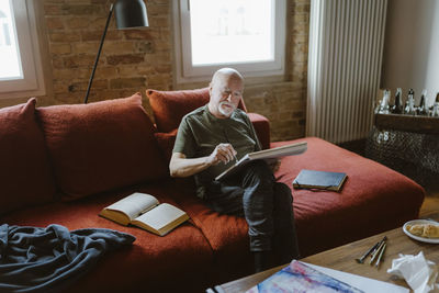 Senior man painting while sitting on sofa at home