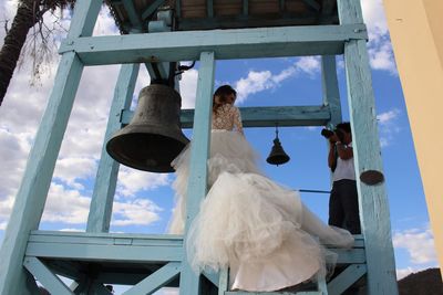 Low angle view of man photographing bride standing by bell