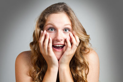 Close-up portrait of shocked young woman with head in hands against gray background