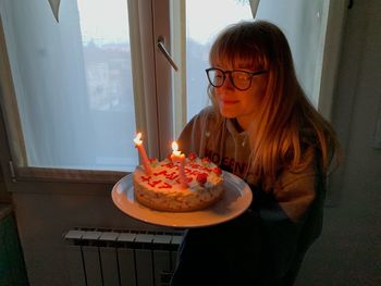 Teenage girl with illuminated birthday cake at home