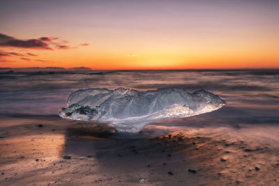 Ice at beach against sea and sky during sunset