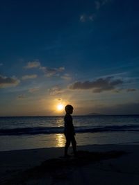 Silhouette boy standing on beach against sky during sunset