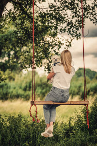 Young woman with a white dog on a tree swing.