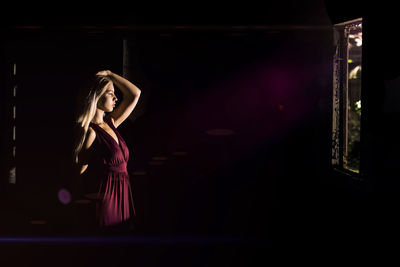 Side view of woman standing against illuminated lights