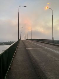 Street lights on road against sky during sunset