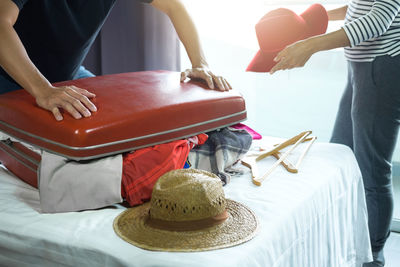 Midsection of man packing suitcase on bed at home