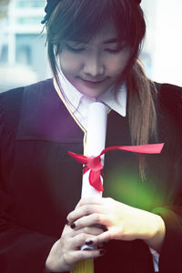 Young woman wearing graduation gown holding certificate