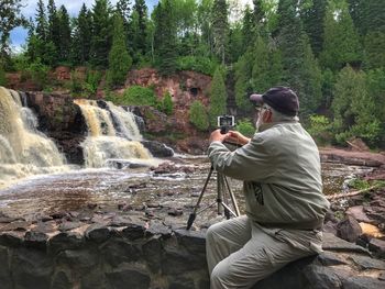 Rear view of man photographing on mobile phone in forest